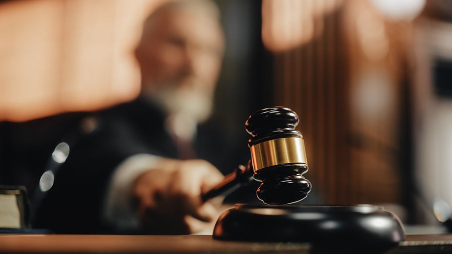 A judge holding a gavel in court, ready to strike it, with a blurred background.